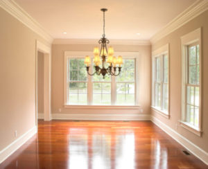 An unfurnished room with a chandelier is brightly lit by walls of windows