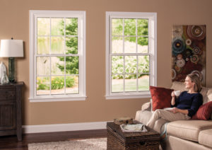 A woman sits on a couch in a living room with a wall of single-hung windows